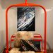 Orange replica chairlift swing indoors with a sheepskin throw and ski print pillows below a skier painting