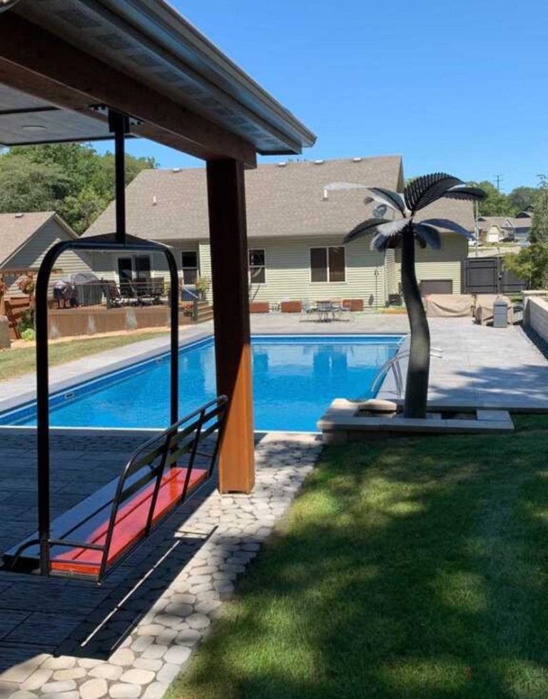 Black powder coated replica chairlift bench with a red seat beside a backyard swimming pool