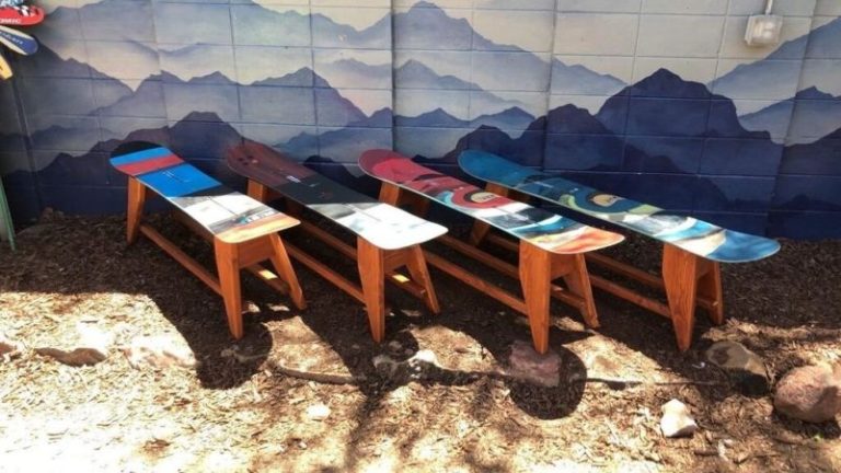 Row of four single snowboard benches in blue, red and teal on stained wood legs