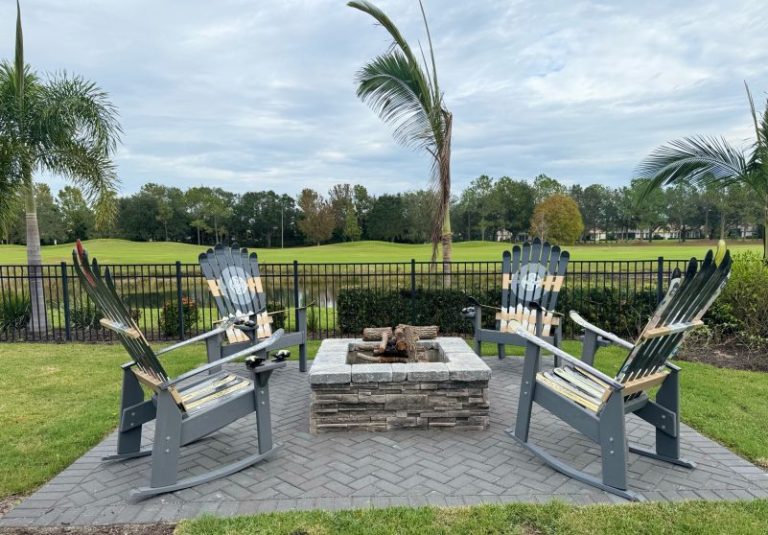 Four grey Adirondack ski rocking chairs circled around a paver fire pit on a golf course lawn