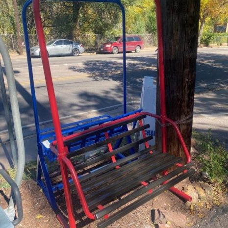 Original two-person chairlift bench in red and blue with a weathered wood slat seat