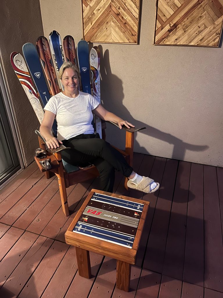 Woman seated in an Adirondack chair made from red, white and blue skis on a patio