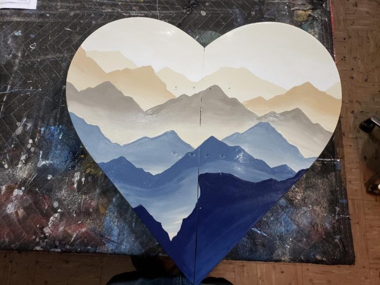 Heart shaped snowboard wall art hand painted with layered blue and tan mountain ranges