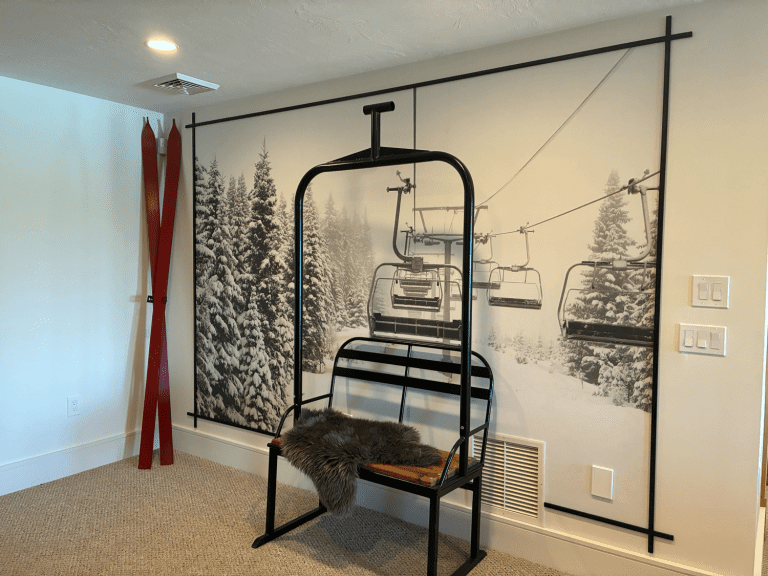 Black powder coated two-person replica chairlift bench in a room with a snowy chairlift wall mural