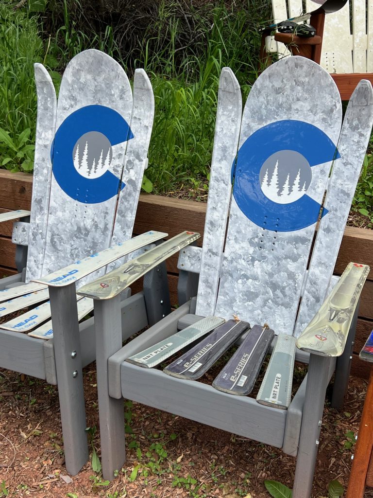 Two grey Adirondack ski chairs with a blue Colorado C and pine trees on the backs