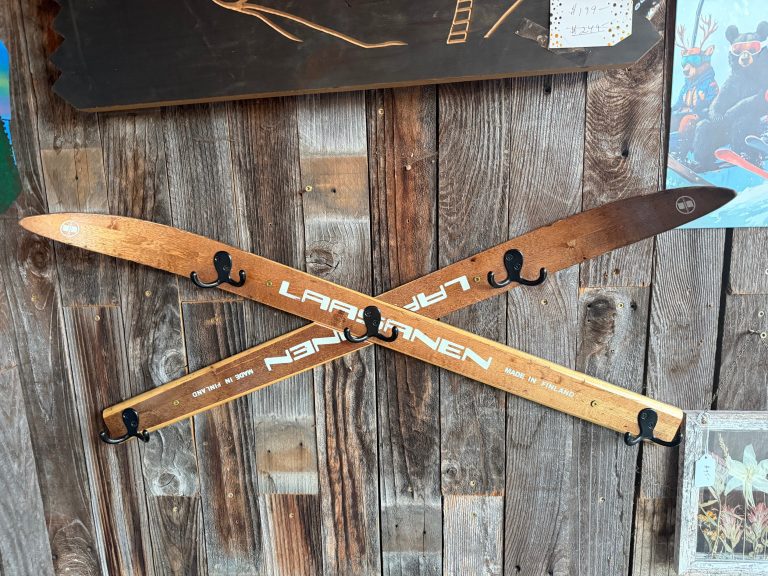 Crossed antique wooden skis mounted as a coat hook with five black double hooks on barn wood