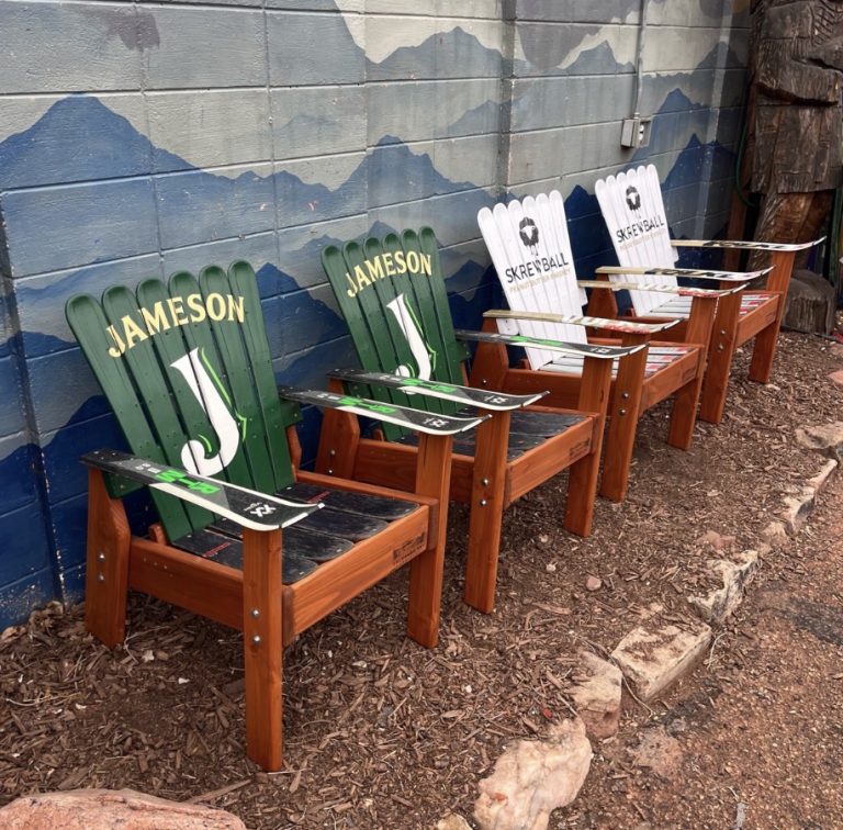 Row of green and white Adirondack ski chairs carrying beverage brand logos along a painted mountain wall
