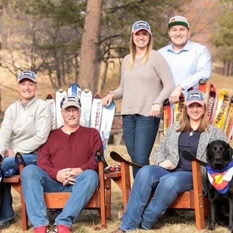 Family and two black labs gathered on ski chairs made from their own skis outdoors